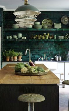 a kitchen with green tiled walls and wooden counter tops, surrounded by potted plants