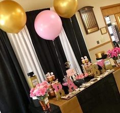 a table topped with pink and gold balloons next to black drapes filled with flowers