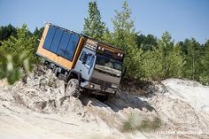 an off road truck driving through the sand in front of some trees and bushes on a sunny day