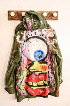 a green jacket hanging on a wall next to a coat rack with an evil face painted on it