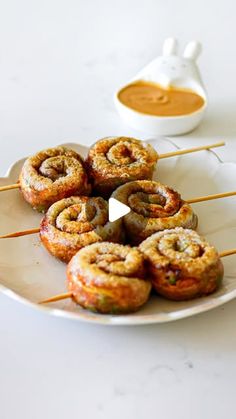 a white plate topped with cinnamon buns on top of a table next to a bowl of dipping sauce