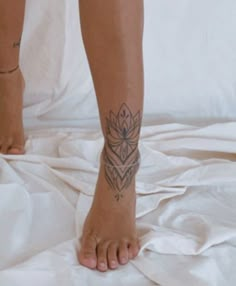 a person with a tattoo on their foot standing on a white sheeted bed spread