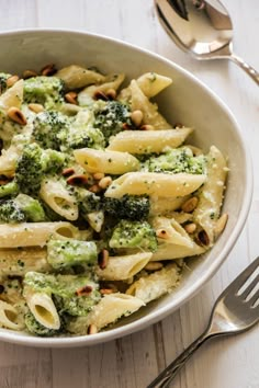 a white bowl filled with pasta and broccoli on top of a wooden table