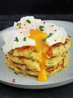 a stack of pancakes topped with an egg and cheese sauce on a white plate sitting on a table