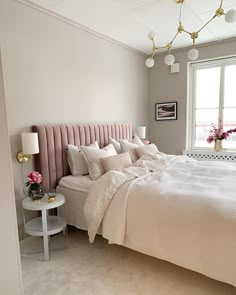 a bedroom with a large bed and pink headboard on the wall next to a window