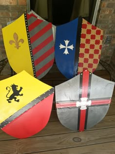 four shields with different colors and designs are sitting on a wooden table in front of a brick wall