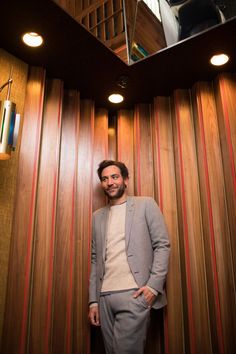 a man standing in front of a wooden paneled wall with lights hanging from the ceiling