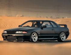 a black car driving down a road in the middle of sand dunes with its hood up