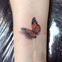 a small butterfly tattoo on the wrist is shown in black and orange colors with white dots