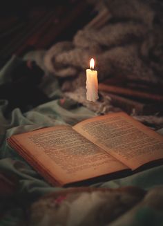 an open book sitting on top of a bed next to a lit candle