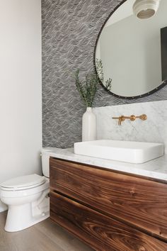 a white toilet sitting next to a bathroom sink under a mirror on top of a wooden cabinet