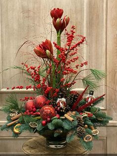 a vase filled with red flowers and greenery sitting on top of a wooden table