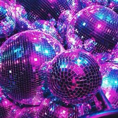 many shiny disco balls are stacked up in a pile with purple and blue lights on them