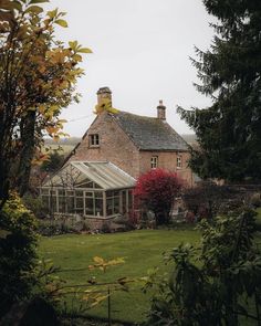 an old brick house with a glass roof and garden area in the foreground, surrounded by trees