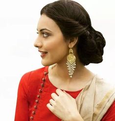 a woman in a red dress with gold earrings on her neck and hand near her chest