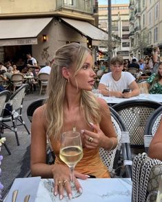 a woman sitting at an outdoor table with a glass of wine in front of her