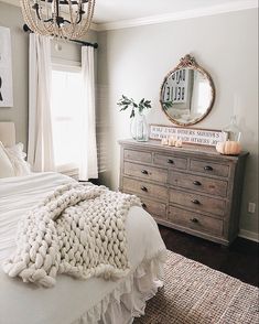 a white bed sitting next to a wooden dresser in a bedroom under a chandelier