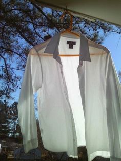 an unbuttoned white shirt hanging on a clothes line with trees in the background