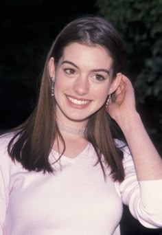 a woman with long brown hair wearing a white sweater and earrings smiles at the camera