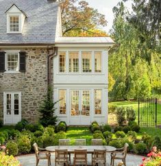 an outdoor dining table and chairs in front of a large stone house with white windows