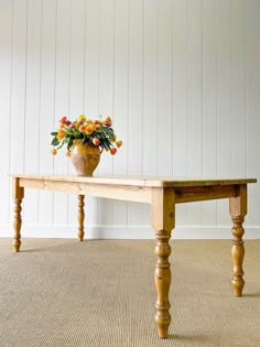 a vase with flowers on top of a wooden table in front of a white wall