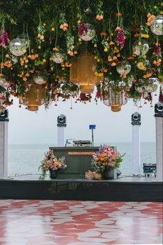 an outdoor stage with flowers and hanging decorations on the ceiling, overlooking the water's edge