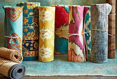 a row of colorful rugs sitting on top of a wooden floor next to rolled up carpet