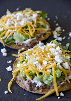 two mini pizzas topped with cheese, lettuce and other toppings on a black surface