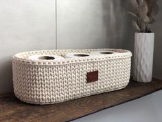 a white basket with two rolls of toilet paper in it sitting on a shelf next to a potted plant