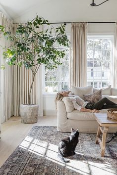 a woman laying on top of a couch next to a black cat in a living room