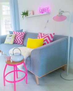 a living room with blue couches, pink and yellow pillows on the back wall