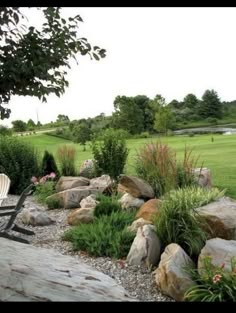 a lawn chair sitting on top of a pile of rocks next to a lush green field