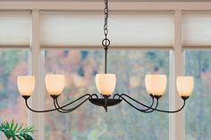 a chandelier with five lights hanging from it's sides in front of a window