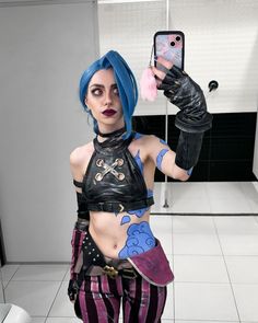 a woman with blue hair and black leather outfit holding up a cell phone in front of her face