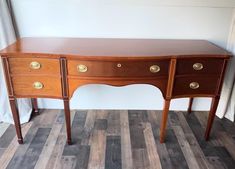 a wooden desk with two drawers and gold knobs on the top, in front of a window