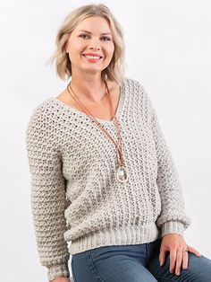 a woman sitting on top of a wooden stool wearing jeans and a sweater with an open v - neck