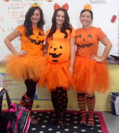 three girls dressed up as pumpkins in front of a whiteboard with writing on it