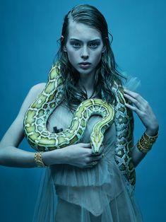 a woman holding a large snake in her hands and posing for the camera with blue background