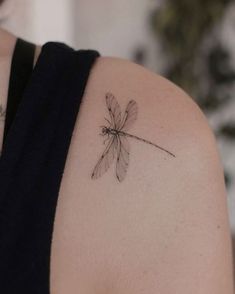 a woman's back shoulder with a small dragonfly tattoo on her left arm