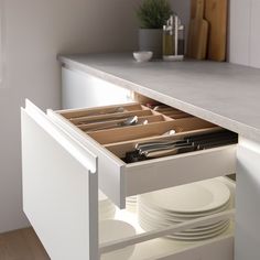 an open drawer in a kitchen with plates and utensils on the bottom shelf