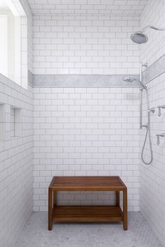 a white tiled bathroom with a wooden bench in the corner and shower head above it