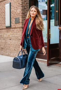 a woman walking down the street carrying a handbag and wearing a red velvet blazer