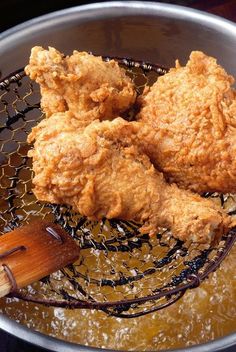 two fried chicken in a frying pan with a wooden spatula