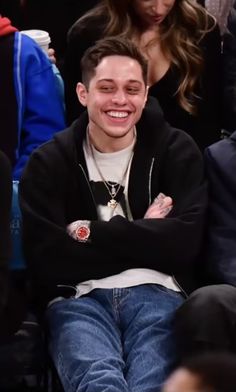 a smiling young man with his arms crossed sitting in front of a group of people