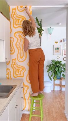 a woman standing on a stool in front of a wall with an orange and white design