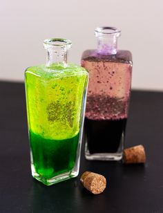 two bottles filled with different colored liquid next to some corks on a black table