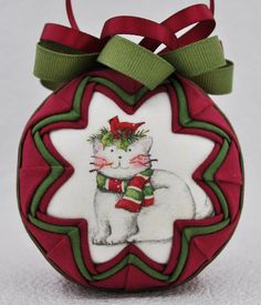 a red ornament with a white cat on it's side and green ribbon around the neck