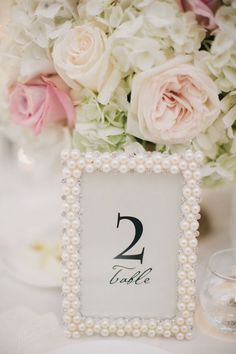 the table numbers are displayed in pearls and glass vases with pink flowers behind them