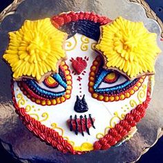 a decorated sugar skull with yellow flowers on it's head and eyes, sitting on top of a silver plate