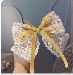 a hand holding a white lace bow with yellow ribbon on it's side and the top part of its head